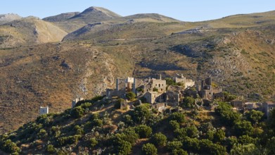 Old buildings of a village embedded in the hilly landscape under a clear blue sky, Vathia,