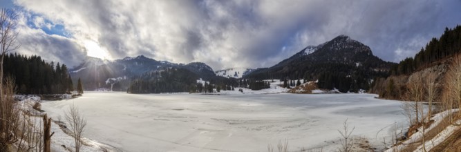Snowy winter landscape with mountains, densely wooded slopes and partly cloudy skies, Spitzingsee