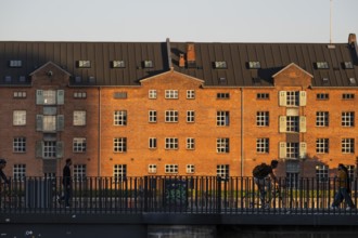 Brick building in the evening light, people and cyclists on a bridge, Christians Brygge,