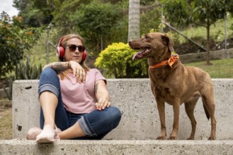 A tranquil woman with headphones sits in the plaza accompanied by her faithful pet