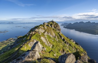 Climber on the summit of Dronningsvarden or Stortinden, behind sea and fjord Umvågsundet,