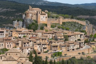 Historic castle overlooking a medieval village, surrounded by green countryside and mountains,