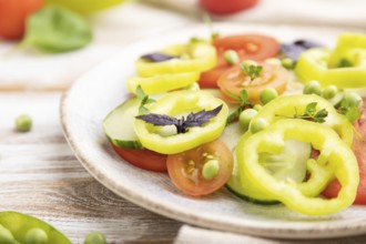 Vegetarian salad from green pea, tomatoes, pepper and basil on white wooden background and linen
