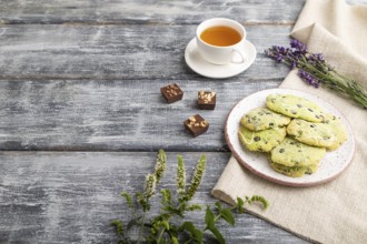 Green cookies with chocolate and mint on ceramic plate with cup of green tea and linen textile on