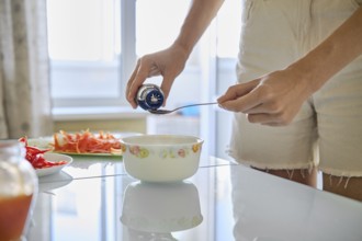An unrecognizable woman adds soy sauce to a bowl while preparing a nutritious meal in a well-lit