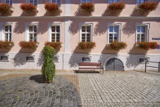 Facade of a light beige-coloured house with windows and flower boxes with blooming geraniums in the