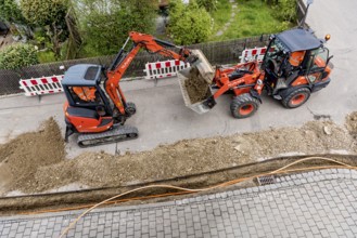 Construction workers laying fibre optic cable in trench under asphalt, cable trench, excavator,