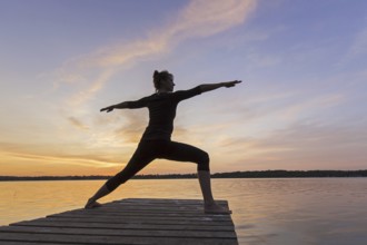 Woman practicing yoga posture Virabhadrasana II, Warrior Pose, lunging standing asana on jetty at