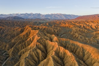 River bed runs through a landscape of eroded hills, badlands at sunset, mountain peaks of the Tian