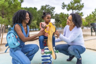 African mother and grandmother holding a girl on a swing in the playground