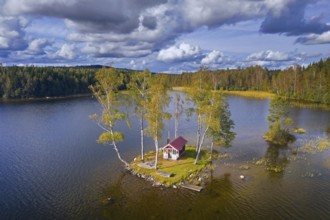 Aerial view over small traditional red wooden cabin on tiny island in lake in autumn, fall,