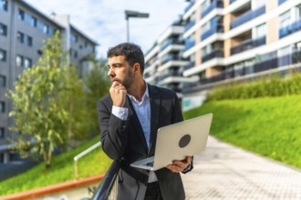 Caucasian adult businessman using laptop standing pensive in the city in a sunny day