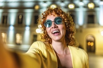 Happy modern female tourist with sunglasses taking selfie in the city at night