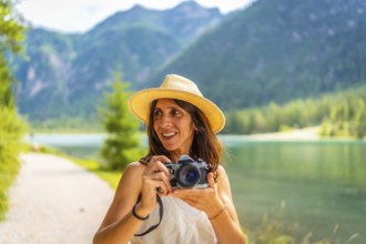 Smiling tourist with straw hat taking photos at lake dobbiaco in the dolomites during summer