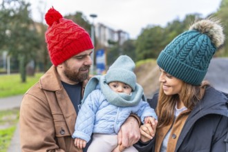 Parents holding their baby while enjoying a leisurely stroll in a park during wintertime, creating