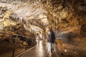 Tourists walking on a concrete footpath inside the famous postojna cave in slovenia, illuminated by