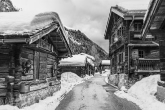 Street with historic old snow-covered wooden houses, black and white photo, mountain village Zinal,