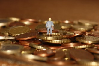 Miniature man sitting among euro coins, North Rhine-Westphalia, Germany, Europe
