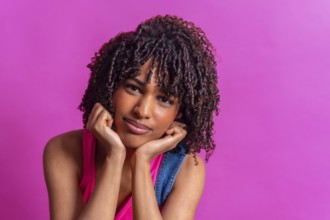 Portrait of a thoughtful young woman with curly hair resting her chin on her hands against a