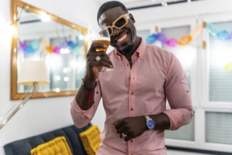 African man wearing sunglasses smiling and toasting at camera during a home party