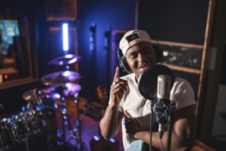 Young black man recording vocals for new album in professional music studio, wearing headphones and