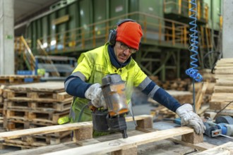 Man with protective gear repairing pallets in a recycling plant warehouse using a compressed air