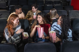Cheerful multi ethnic friends enjoying popcorn while watching a film together in a cozy movie