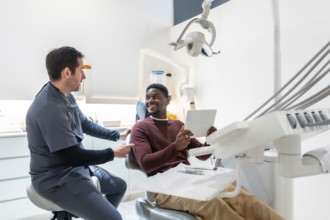 Dentist shows the results of a dental checkup to a smiling patient on a tablet in a modern, bright
