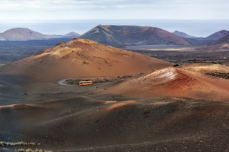 Orange-coloured coach with tourists drives through the fire mountains of Timanfaya National Park,