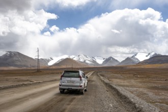 Off-road vehicle on a gravel track, glaciated and snow-covered peaks, Ak Shyrak Mountains, near