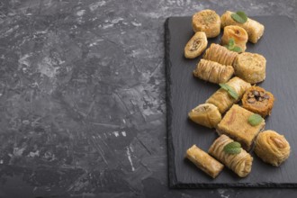 Traditional arabic sweets (kunafa, baklava) on a black slate board on a black concrete background.