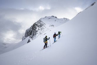 Three ski tourers in a snowy mountain landscape in the morning light, ascent to the Wildhorn,