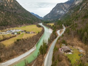 View of a river with a road leading through a green wooded area, surrounded by mountains and cloudy
