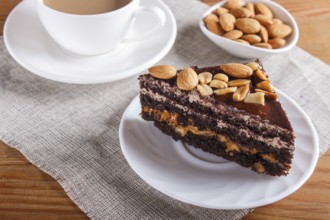 Chocolate cake with caramel, peanuts and almonds on a brown wooden background. cup of coffee, top