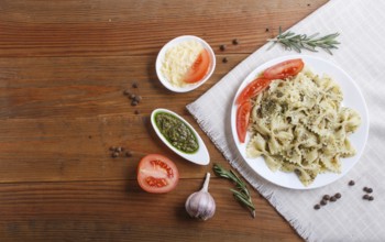 Farfalle pasta with pesto sauce, tomatoes and cheese on a linen tablecloth on brown wooden