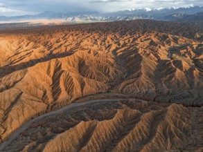River bed runs through a landscape of eroded hills, badlands at sunset, mountain peaks of the Tian