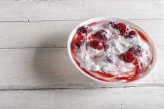 White plate with greek yogurt and strawberry jam on white wooden background. close up. copy space