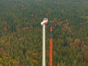 Close-up of a crane and a wind turbine in autumn forest, wind farm construction site, Grömbach,