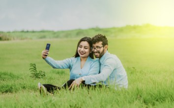 Smiling young couple in love taking a selfie sitting in the field. Happy Couple in love taking a