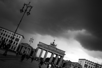 People visit the Brandenburg Gate on a day with a threatening, dramatic sky and heavy clouds, light