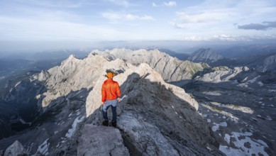 Mountaineer on a narrow rocky steep ridge, view of the Höllental and the Alpspitze from the