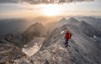 Mountaineer with helmet on a narrow rocky ridge at sunrise, crossing the Jubiläumsgrat, view of
