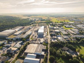 Numerous buildings and streets in an industrial area, surrounded by wooded landscape under a sunny