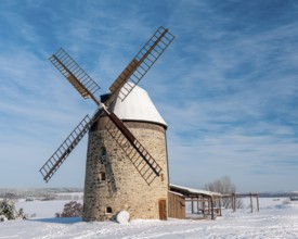 The tower windmill of Warnstedt in winter surrounded by snow-covered landscape under a blue sky,