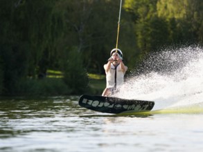 Sporty young man with helmet and waistcoat on wakeboard in lake, water sports, water skiing in