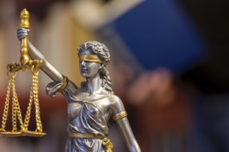 Close-up of a Justitia, in the background a man is reading a book (symbolic image)