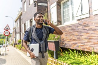 African young businessman talking to the mobile going to work walking along a residential street