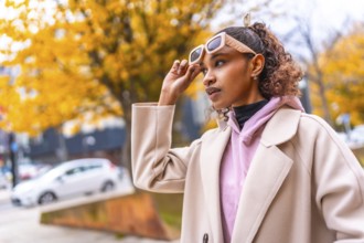 Confident young african woman with sunglasses and coat in the city in a cold day of autumn