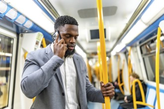 Young businessman having phone call while commuting on subway train, holding onto handrail