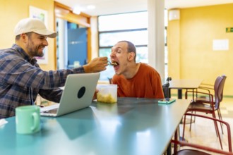 Caucasian male colleague feeding a man with disability in a coworker cafeteria